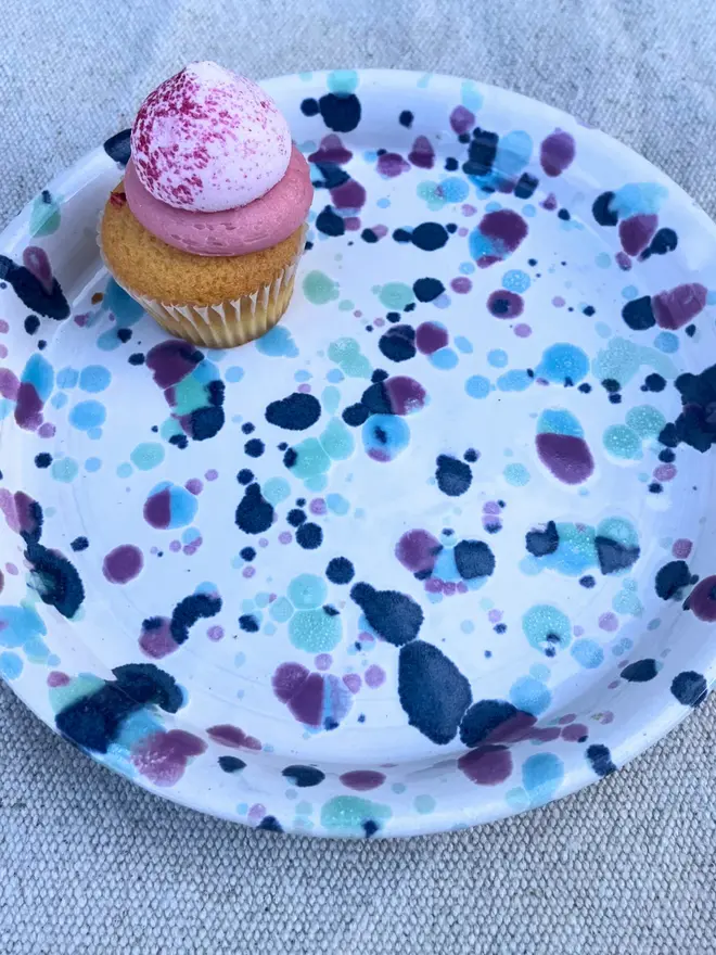 Sweetpea Side Plate, a colourful plate on a stone surface. It is accompanied by a sweet treat. 
