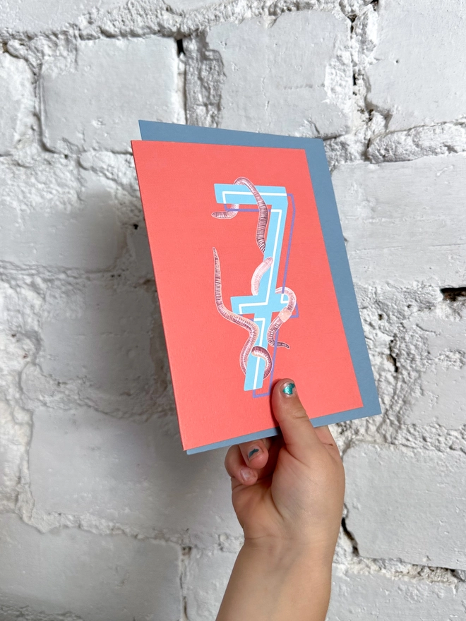 a bright red card with a big blue number 7 and some illustrated earthworms with a blue envelope