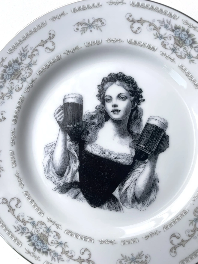 a vintage plate with an ornate border, in the centre of the plate is a vintage style black and white illustration of a Bavarian Oktoberfest German barmaid holding two pints of beer
