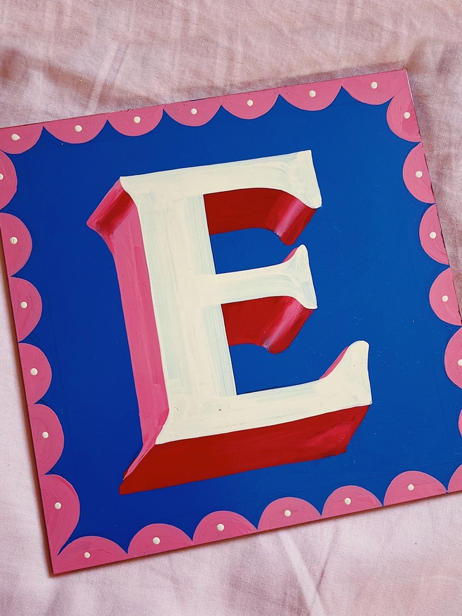 Blue background 'E' with ivory lettering, red and pink shade and border.