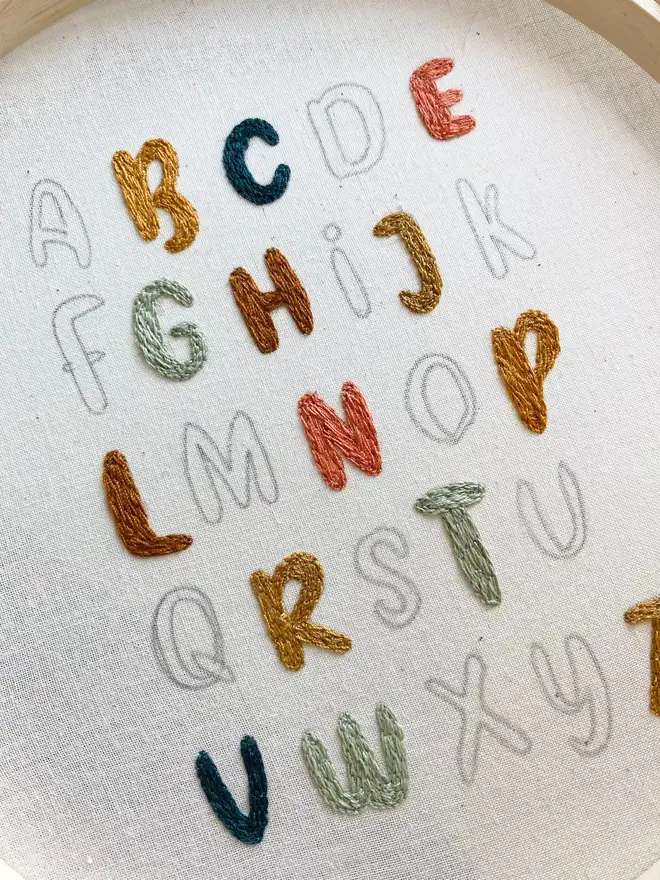 letters of the alphabet embroidered hoop. colourful stitch alphabet hoop during making process.