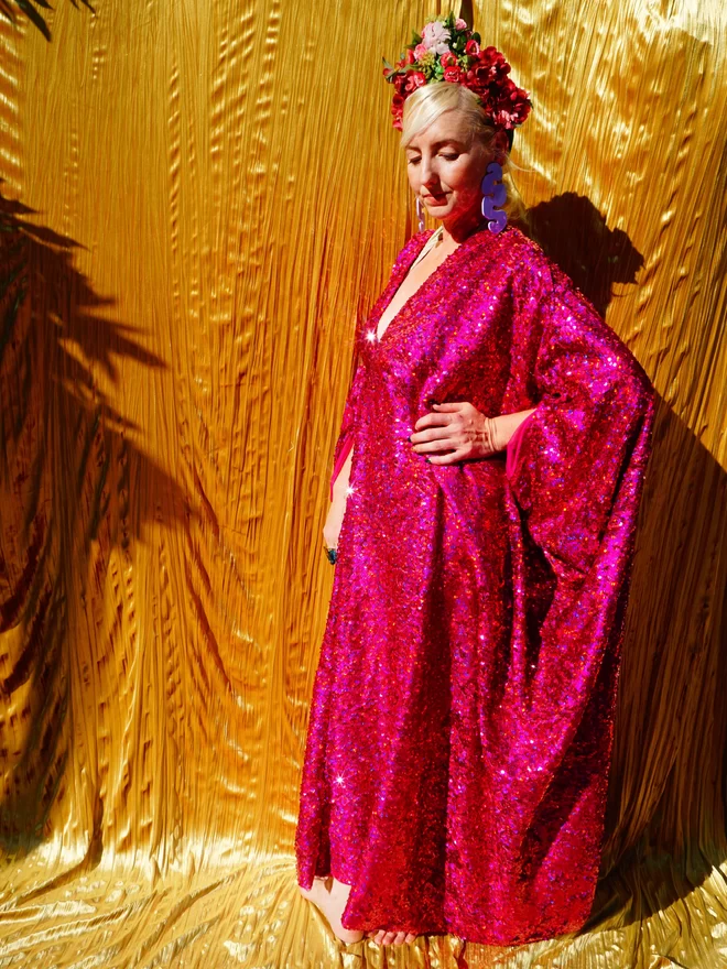 Cerise Holographic Sequin Kaftan seen on a woman standing with her hands on her hips.