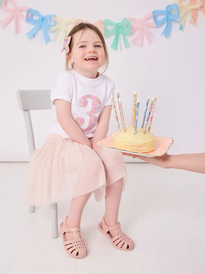 a 3 year old girl wearing a white birthday t-shirt with a number 3 cut from liberty floral print on the front