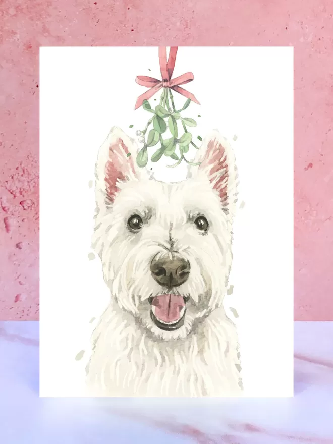 A Christmas card featuring a hand painted design of a Westie, stood upright on a marble surface.