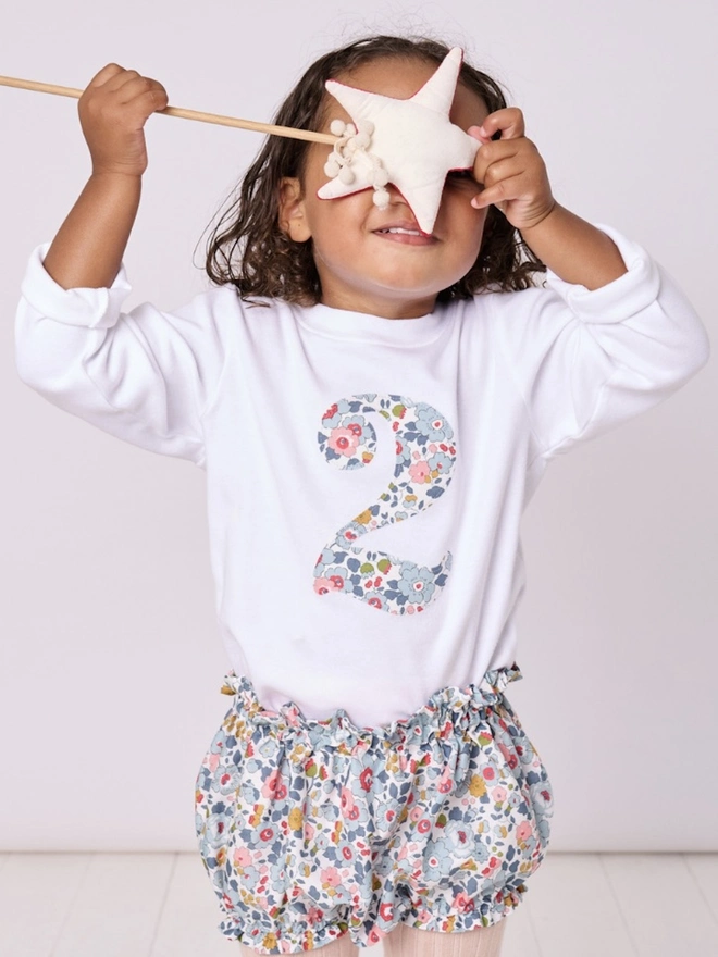 a 2 year old girl wearing a white birthday t-shirt with a number 2 cut from liberty floral print on the front