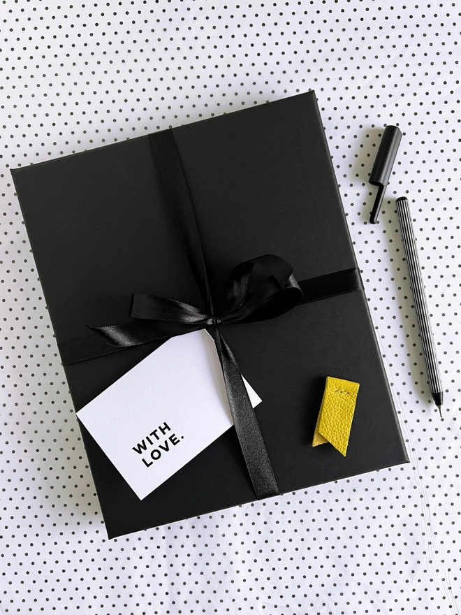 Wrapped black gift box with black ribbon, gift card, yellow marker, and black striped pen