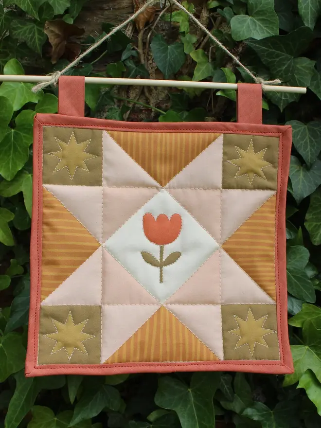 tulip quilt wall hanging. a patchwork quilt with a pink star pattern in the centre and embroidered tulip.