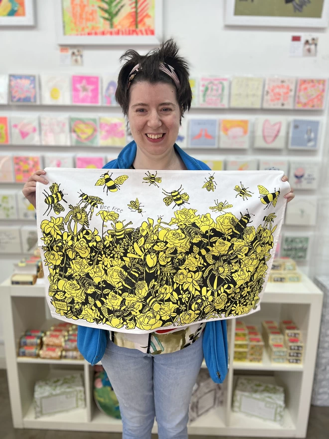 Smiling artist holding bee free 100% organic cotton charity tea towel in arthouse unlimited studio 
