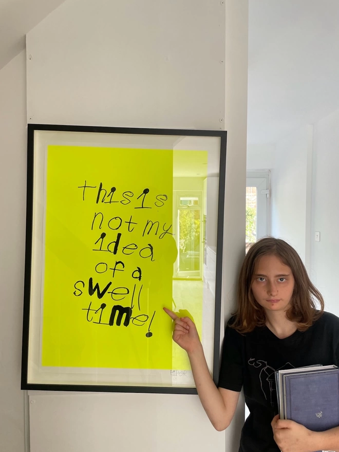 Piper pointing to her framed screen print which is in neon yellow with black in