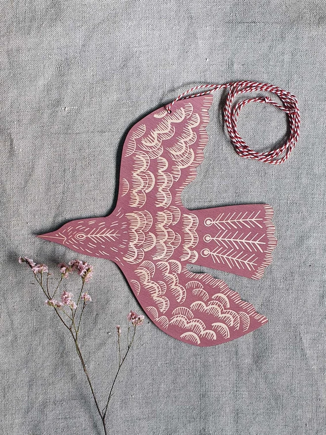 Hanging wooden hand printed bird decoration in a rose pink colour.