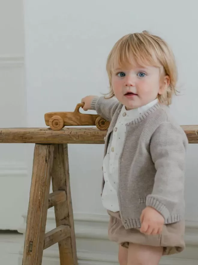 a little baby playing with the wooden white car toy