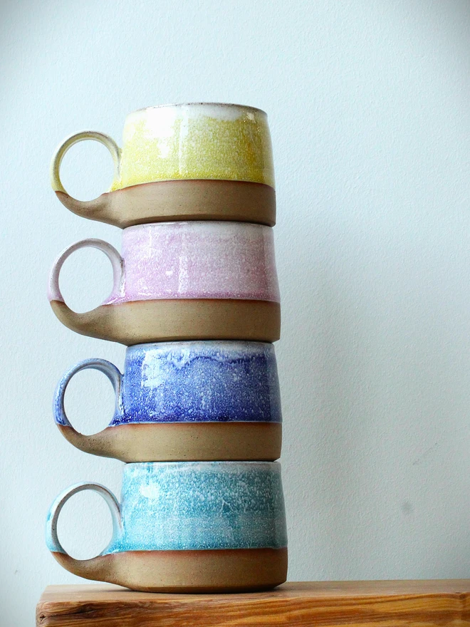 Four handmade ceramic cups with pastel glazes—blue, yellow, teal, and pink—
