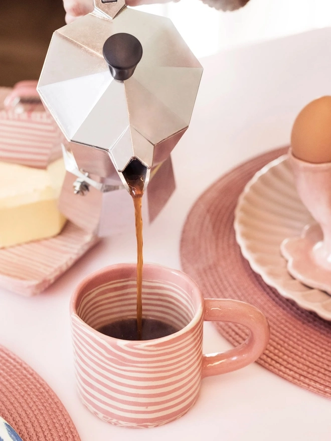 Pink Striped Mug, a pink striped mug being poured coffee into on a white table surface. It is accompanied by other colourful ceramics. 