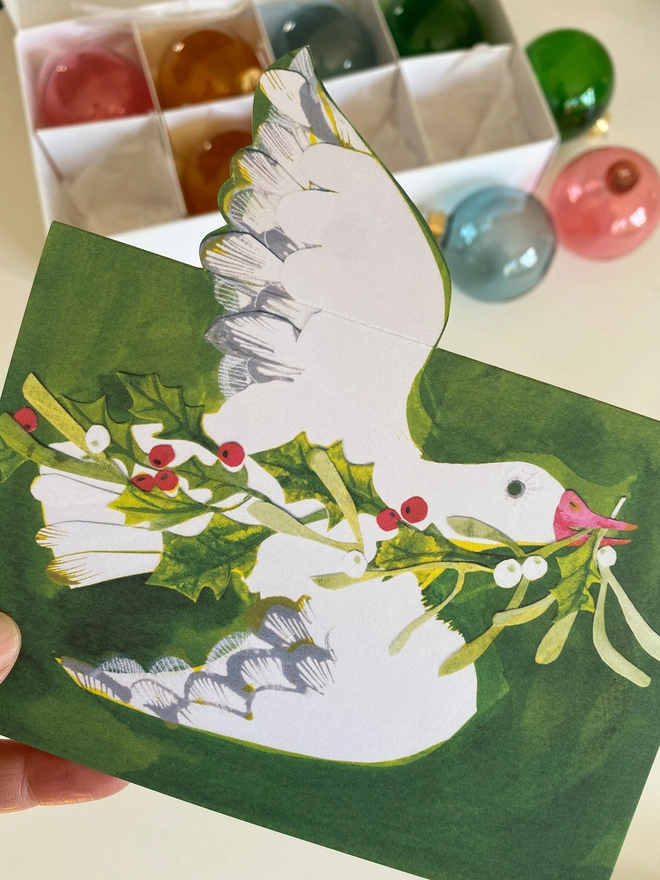 Esther Kent illustrated Christmas Card showing white goose on green inky background, carrying holly and mistletoe