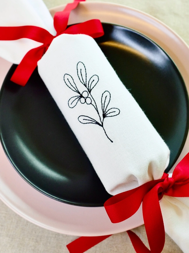 White cotton Christmas cracker with embroidered mistletoe design and red ribbon bows 