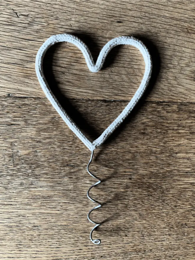 A white string wrapped wire heart shaped Christmas tree topper on an oak table