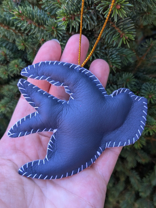 The navy blue reverse of a hand stitched personalised swallow Christmas decoration made from vegan-friendly faux leather and velvet, featuring gold stars, festive holly and a cream banner personalised with a name, hanging from a gold cord on a Christmas tree.