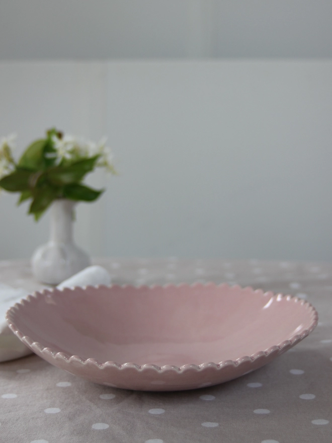 pink scalloped edge serving bowl for fruit or salad on a table top with a flower vase in background