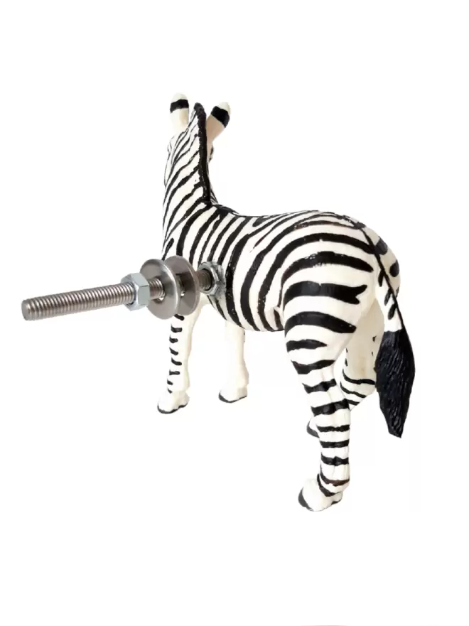 A zebra safari animal door knob on a white background. The fixing bolt, nut and washers of the zebra knob can be seen protruding out the back of the zebra. The zebra knob 9cm tall, it is made of plastic with metal fastenings, the brand of the animal door knobs is Candy Queen Designs.