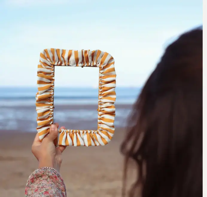 Soft ruffled frames with mustard-and-white striped fabric trim being held on the beach. 