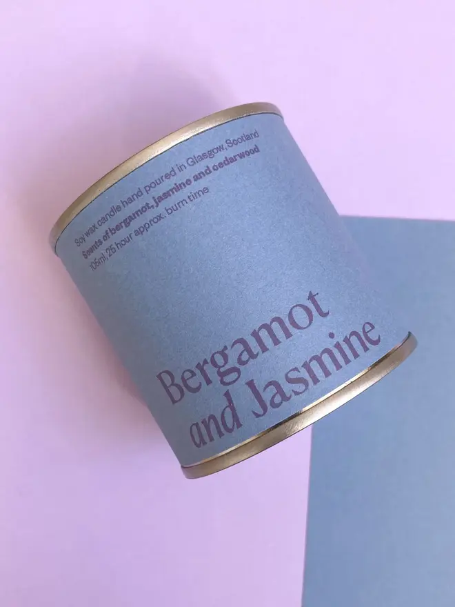 Bergamot & Jasmine Soy Wax Candle Tin against a purple and blue background. 