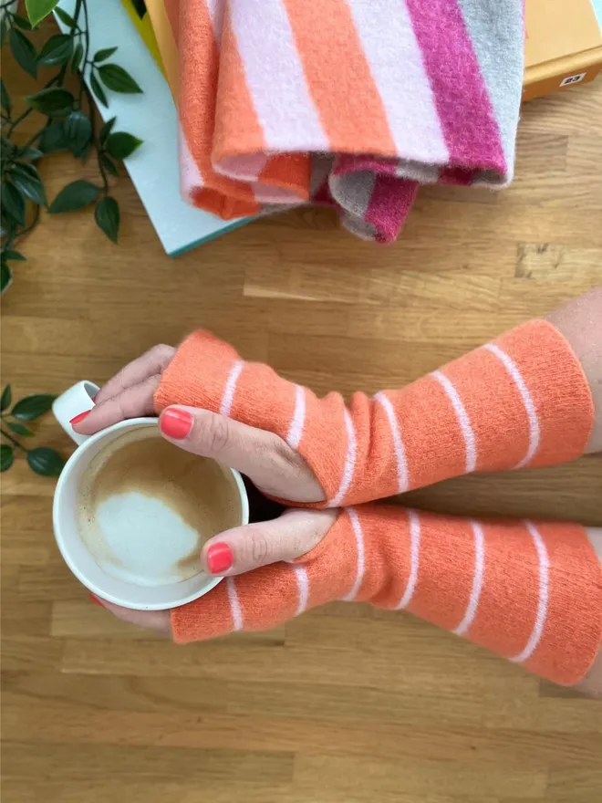 Colourful orange wristwarmers being worn while holding cup of coffee