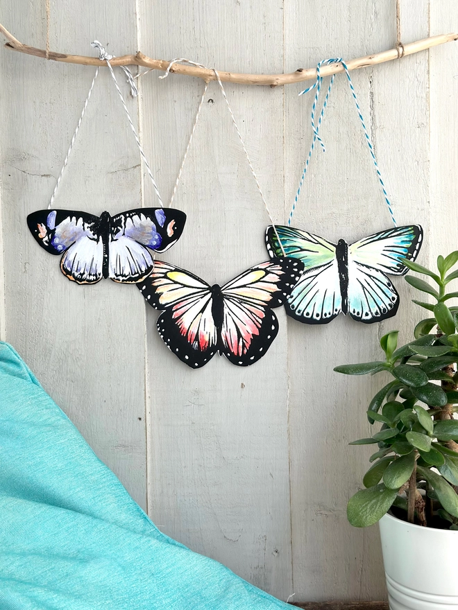 3 Hand Painted Butterflies. Set Of Linocut Wall Hangings displayed on a stick. Colours are purple and peach and teal  