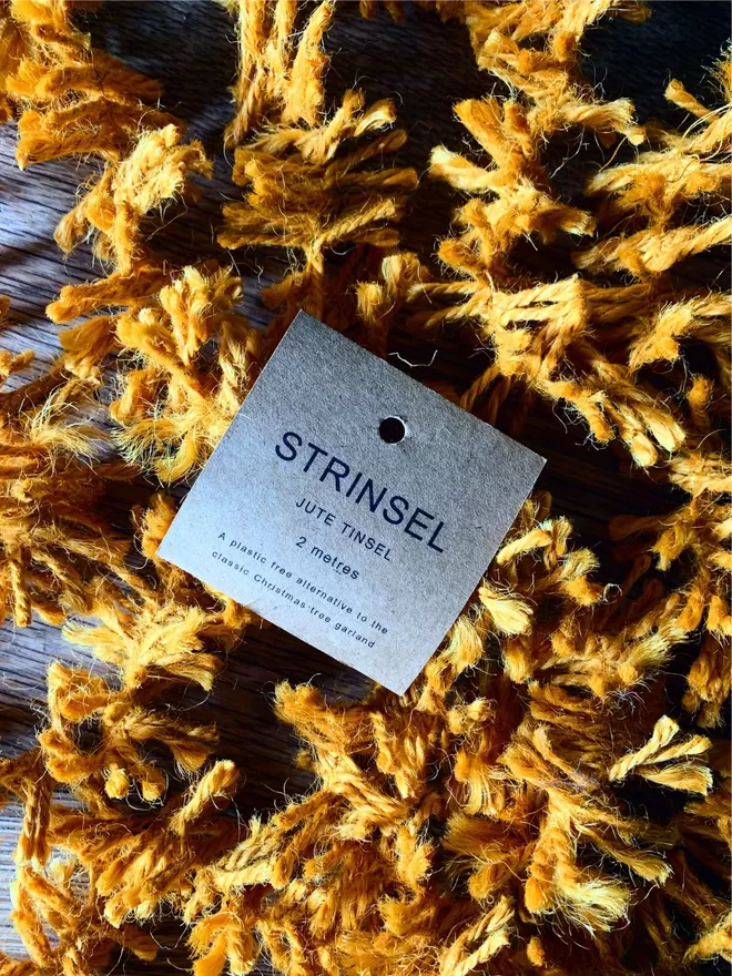 A tumble of Warm Gold  jute string tinsel AKA Strinsel packaged in a kraft card label on an oak table