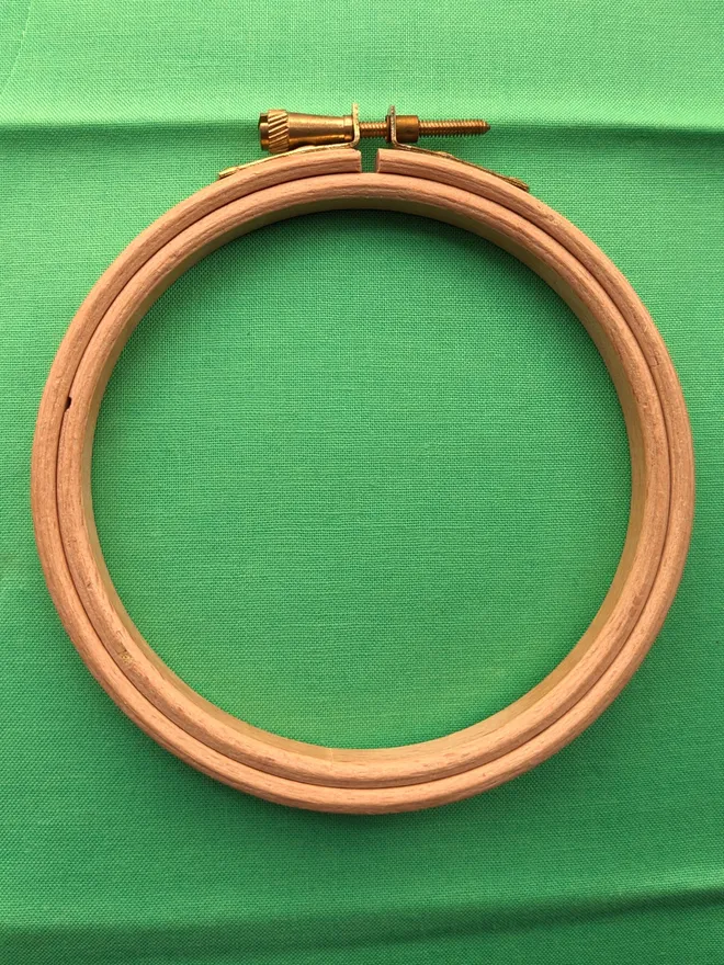 A wooden embroidery hoop lying on a piece of green coloured fabric