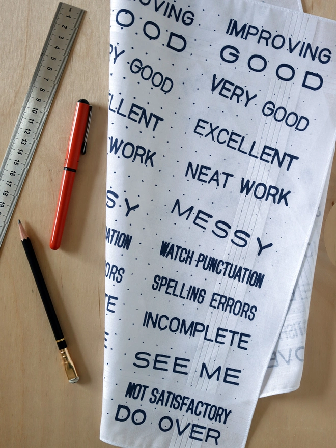A Mr.PS Teacher Handkerchief folded on a tabletop alongside a ruler, pen and pencil