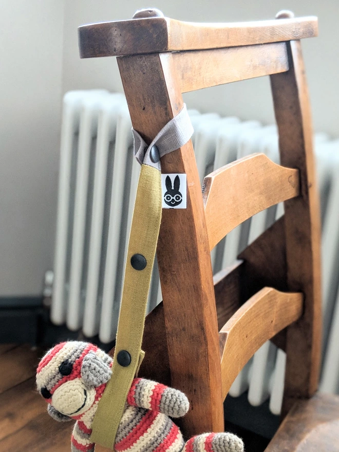 Handmade toy strap in grey and green, attached to a chair on one side and crochet monkey doll on the other side. 