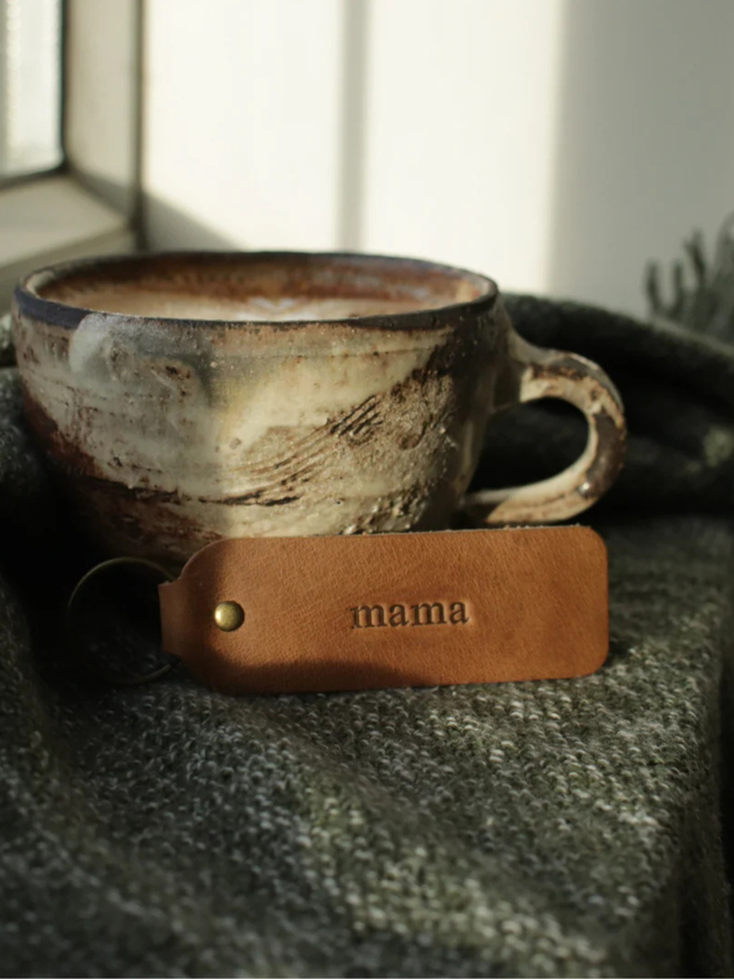 mother's day leather keyring. a brown leather keyring propped up against a coffee cup, embossed with 'girl mom'.