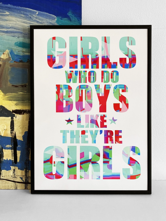 Framed multicoloured typographic print of a Blur song lyric from Girls and Boys - “Girls who do boys like they’re girls”.  The print rests against a blue and yellow abstract painting.