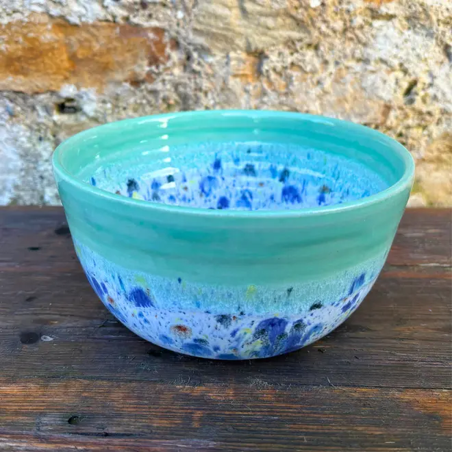 Shoreline Ramen Bowl, a colourful ramen bowl placed on a wooden surface against a brick backdrop. 