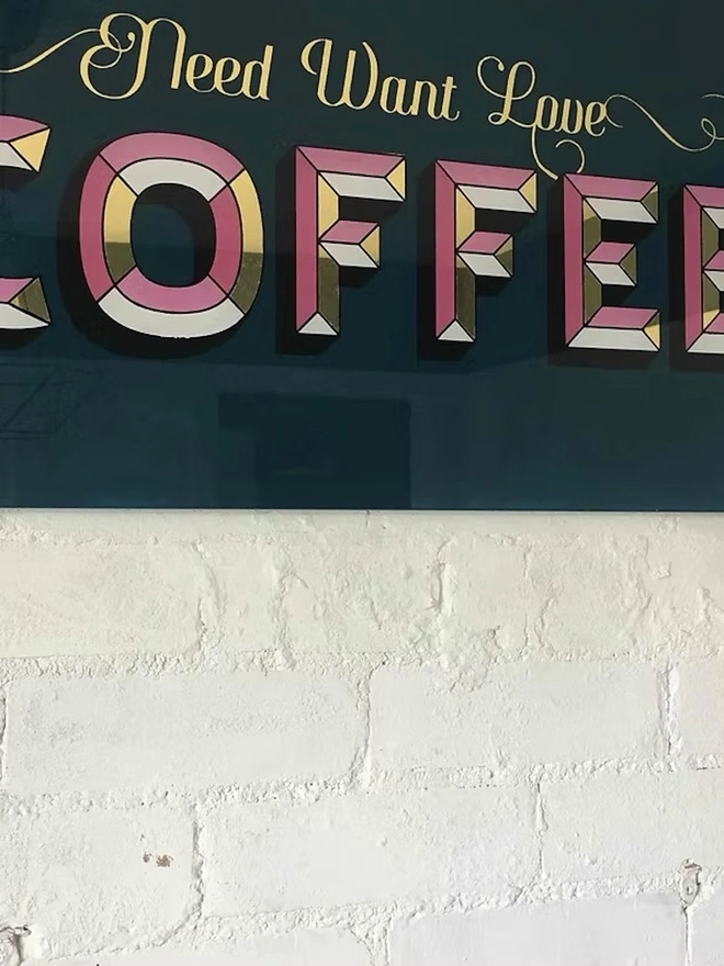 'Need Want Love Coffee' Gold Glass Sign, a gold glass sign hanging on a white brick wall. 