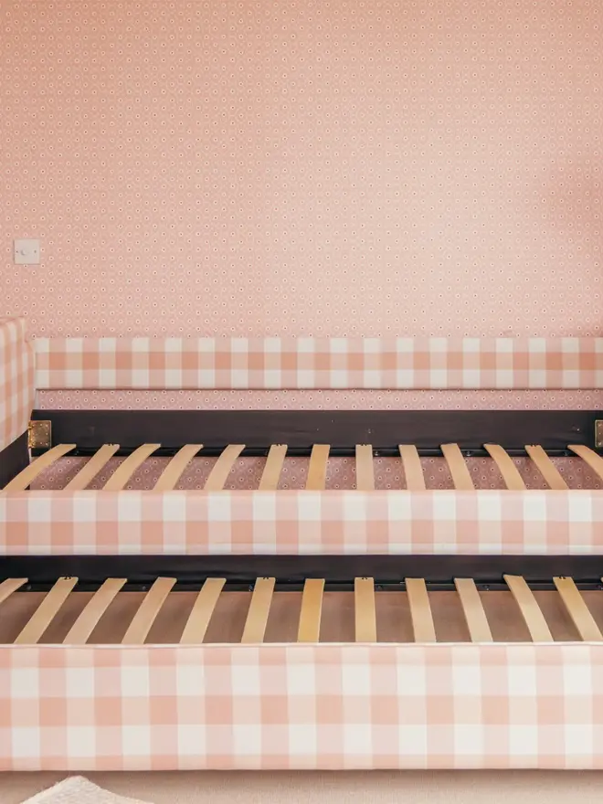 'the posie' pink gingham upholstered children's bed. a pink gingham sofa-style bed, with cushions and bedding removed to show interior slats and trundle bed.