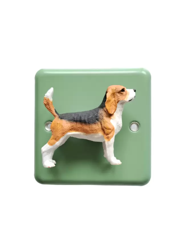 A beagle dog dimmer light switch. The light switch has a pastel green steel metal epoxy coated light switch plate, the beagle dog  is black, brown and white and is made of plastic. The light switch is brand is Candy Queen Designs and Varilight. The beagle dog light switch light switch is on a plain white background.