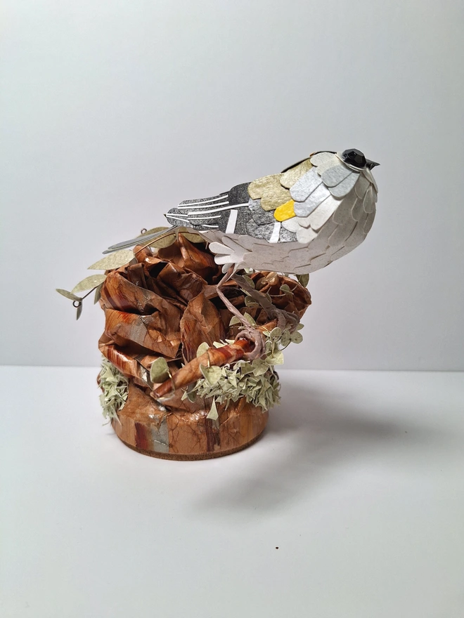 Firecrest paper bird sculpture, perched on a tree stump.  Side view.