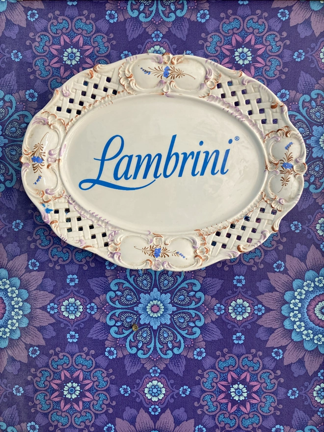 Large, cream oval vintage plate with a blue Lambrini logo in the centre.