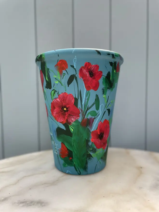 Unique hand-painted terracotta pot featuring red poppies on a royal blue background