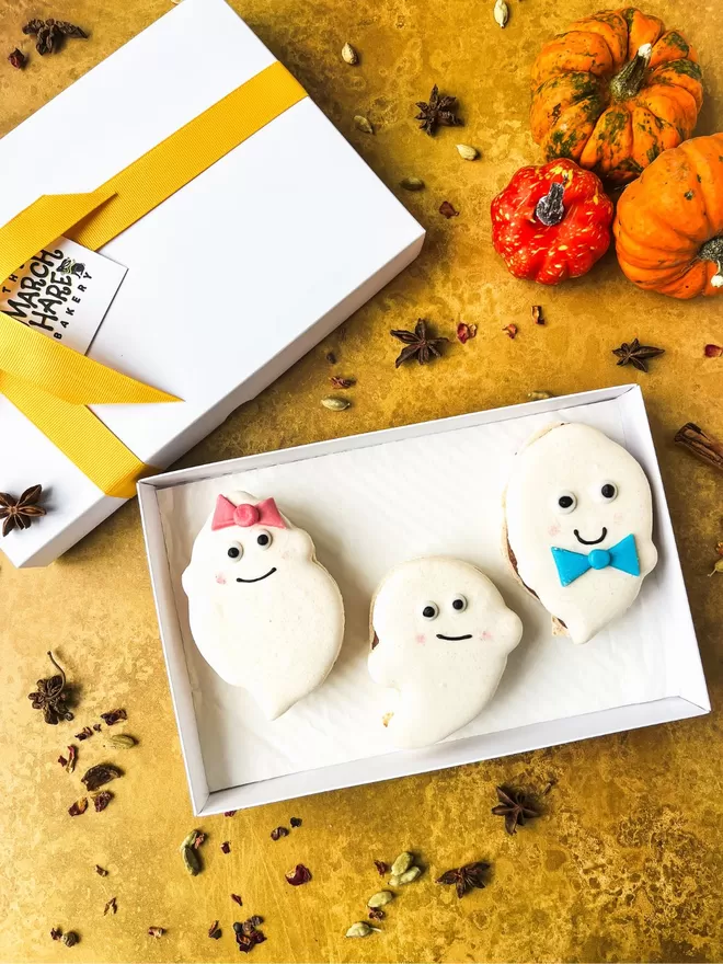 an assortment of halloween ghost macarons on a gold background