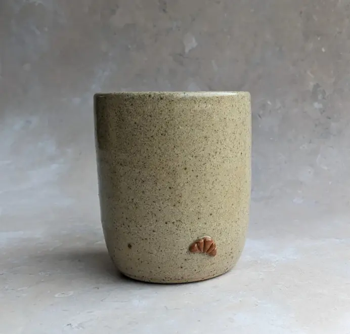Biscuit coloured croissant coffee cup with a subtle croissant design, placed against a grey marble background.