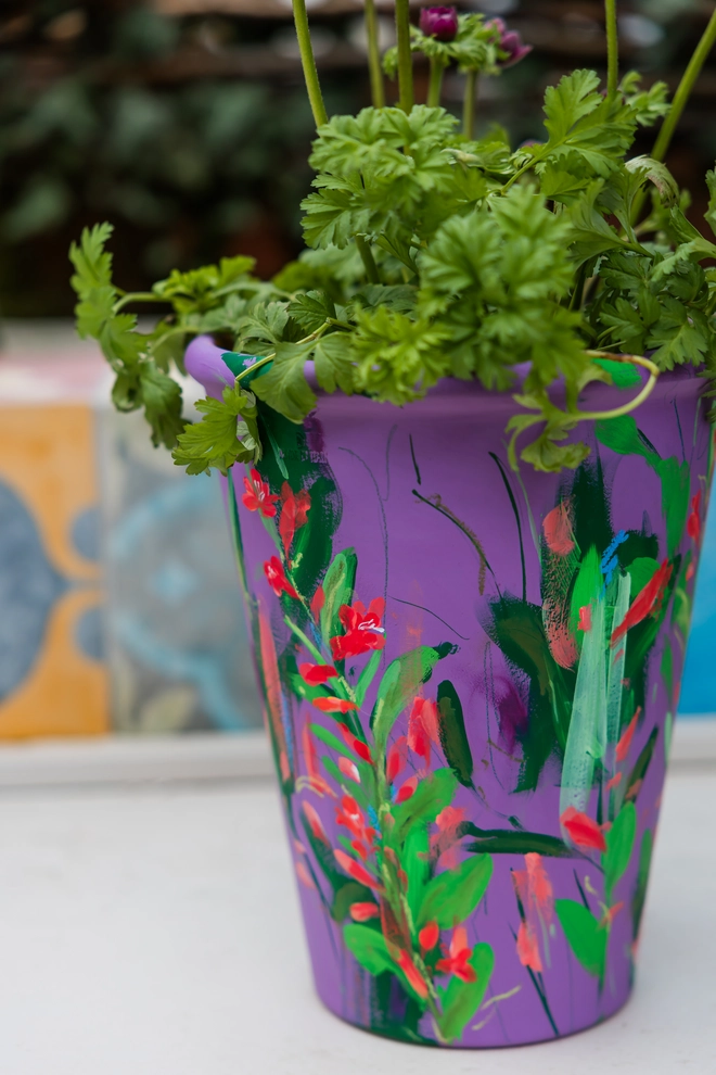 Unique hand-painted terracotta pot featuring twizzle coral flowers on a purple background