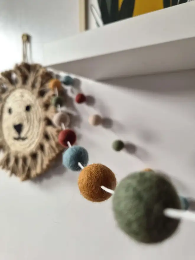 Boho felt ball garland hanging underneath a white shelf.
