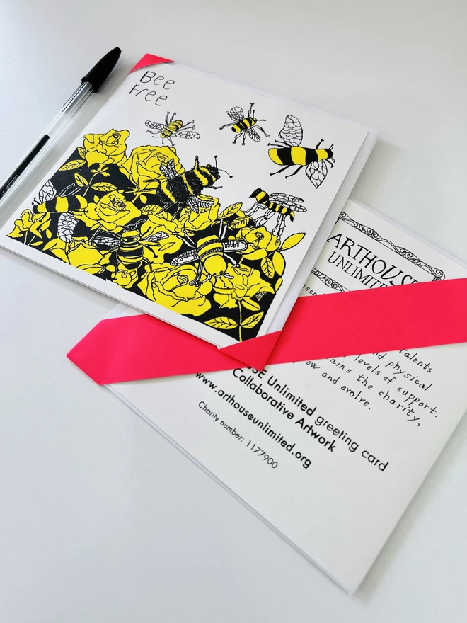 A close up of a riso printed charity card featuring a yellow & black Bee design & the words Bee Free