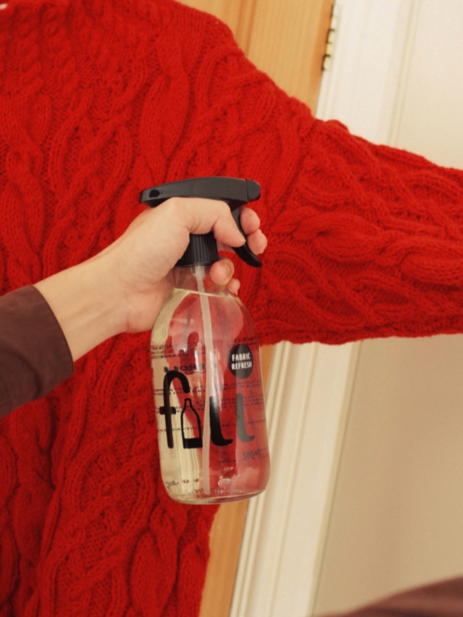 Fabric Refresh. A person spraying a clear bottle labelled Fill Fabric Refresher.