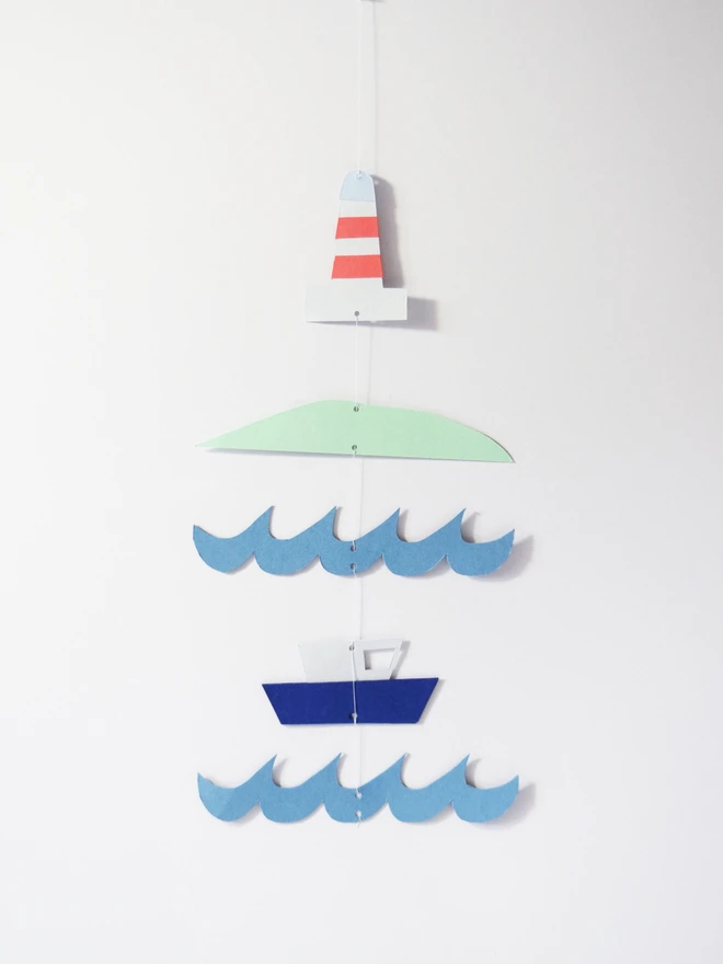 A paper mobile with a lightouse, landscape, sea and boat. Laying against a wall