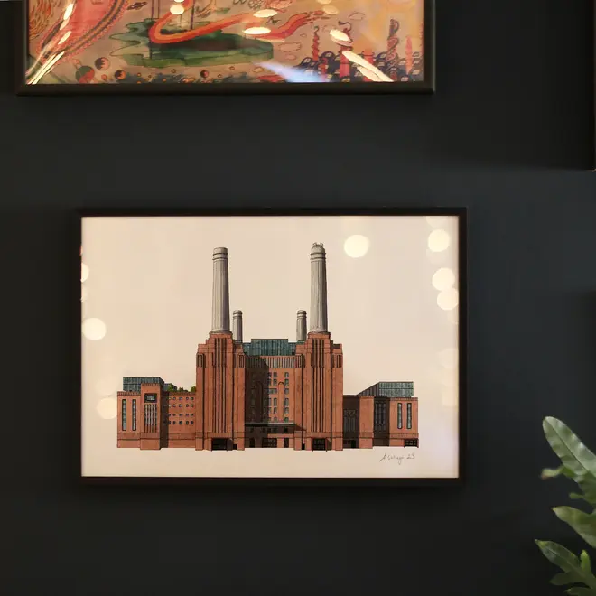 Battersea Power Station Giclée Print (Unframed), a print of Battersea Power Station sitting in a black frame against a black backdrop. It is joined by other framed prints. 