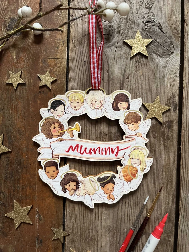 a wooden personalised wooden Christmas wreath featuring a hand painted message and my original illustration called chorus of angels drawn in a vintage traditional story book style