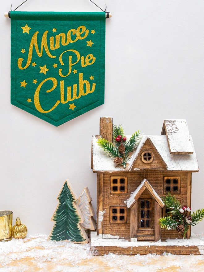 Christmas "Mince Pie Club" banner in holly green felt with yellow gold glitter text. the text is surrounded by glittery stars.. 